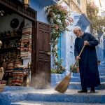 Shopkeeper sweeping Chefchaouen blue medina street